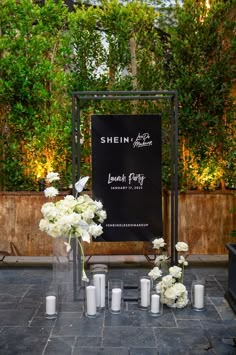 white flowers and candles are arranged in front of a black sign