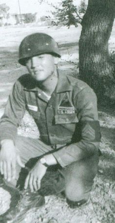 black and white photograph of a man in uniform kneeling next to a tree