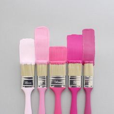 five different colors of paint brushes lined up in a row on a gray background with one pink, the other white