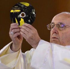 a man holding up a disc in front of his face while wearing glasses and a priest's robe