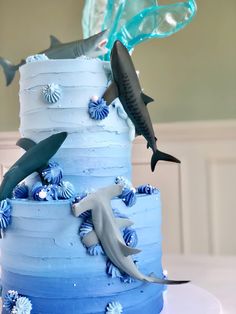 a three tiered cake with blue frosting and sharks on top, surrounded by seashells