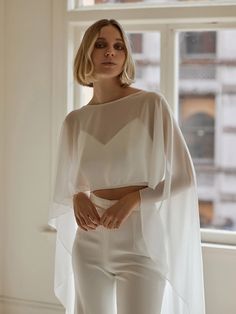 a woman standing in front of a window wearing white pants and a cropped top