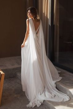 a woman in a white dress is standing near a couch and looking out the window