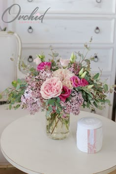 a vase filled with pink flowers sitting on top of a table next to a white dresser