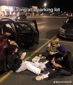 some people sitting on the ground eating food and talking to each other in front of a car