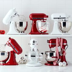 several red and white mixers lined up on a counter top next to each other