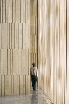 a man standing in front of a wall with wooden slats on the side and his back to the camera