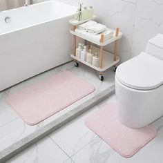 a white toilet sitting next to a bath tub and a pink rug on the floor