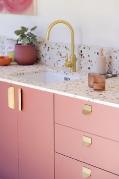 a kitchen with pink cabinets and marble counter tops, gold faucets and potted plants