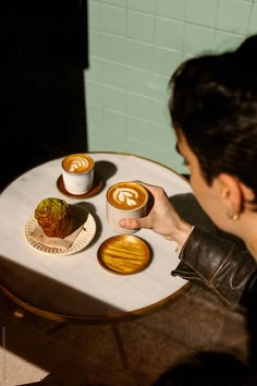 a woman is sitting at a table with two cups of coffee and some cookies on it