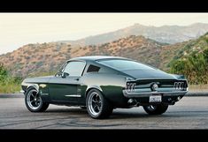 an old muscle car is parked on the side of the road in front of mountains