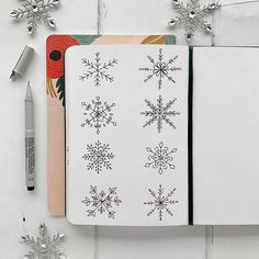 an open notebook with snowflakes on it next to a pen and some christmas decorations