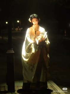 a woman dressed in traditional japanese clothing standing on the street at night with her cell phone