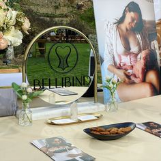 a table topped with pictures and vases filled with flowers next to a round mirror