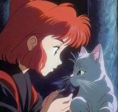 a woman with red hair holding a cat in her hand and looking at it's face