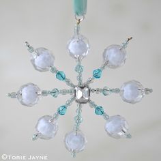 a glass snowflake ornament hanging from a light fixture with blue beads