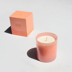 a pink candle next to a box on a white surface with a shadow from the candle