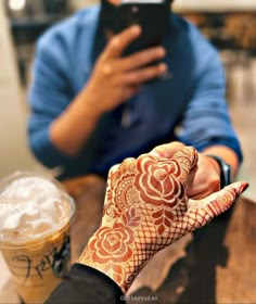 a person with henna on their hand holding a cell phone next to a drink