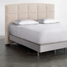 an upholstered bed with white linens and pillows on it's headboard