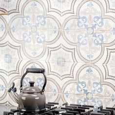 a tea kettle sitting on top of a stove in front of a wall with tiles