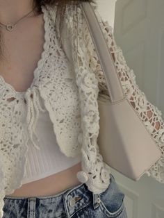 a close up of a person holding a handbag and wearing a white top with lacy sleeves