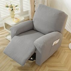 a grey recliner chair sitting on top of a hard wood floor next to a window