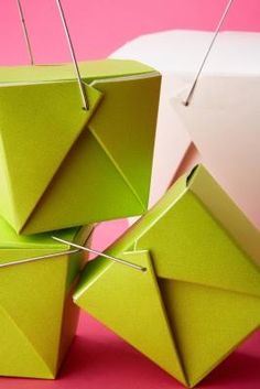 four green origami cubes with pins sticking out of them on a pink background