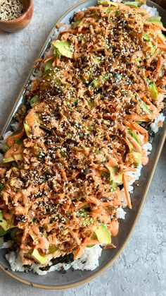 a platter filled with sushi and vegetables on top of rice next to a bowl of seasoning