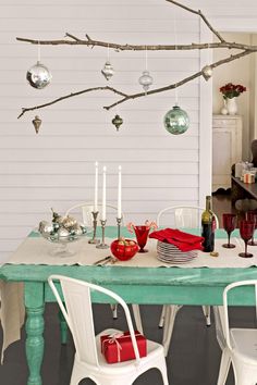 a dining room table with white chairs and christmas ornaments hanging from the branches above it