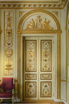 an ornately decorated doorway with red chair in the foreground and gold trimming on the walls