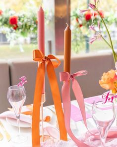 the table is set with pink and orange flowers in vases, candles, and napkins