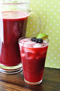 two glasses filled with red drinks sitting on top of a wooden table