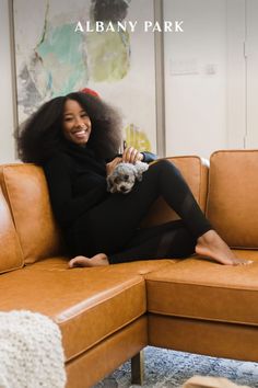 a woman sitting on top of a brown couch holding a small dog in her lap