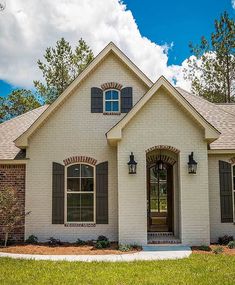 a white brick house with shutters on the front and side windows, surrounded by green grass