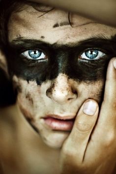 a man with black face paint holding his hands to his face and looking at the camera