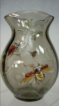 a glass vase with bees and flowers painted on the side, sitting on a white surface