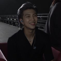 a young man sitting on top of a red couch next to a person wearing ear buds