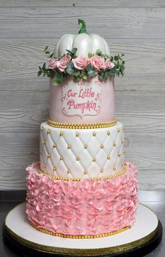 a three tiered cake decorated with pink and white frosting, pumpkins and roses