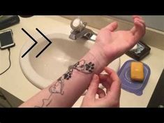 a person with a dog paw tattoo on their arm next to a sink and cell phone