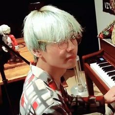 a man with green hair and glasses sitting in front of a piano playing the keyboard