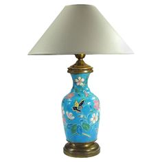 a blue vase with flowers and butterflies painted on it is next to a white lamp