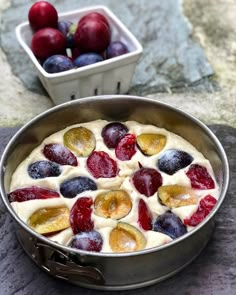 a metal pan filled with fruit on top of a stone counter next to a bowl of cherries