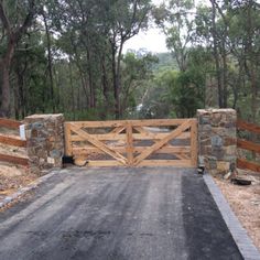 a gated driveway leading into a wooded area with stone walls and wooden gates on either side