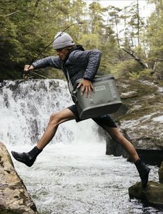 a man jumping over a waterfall while carrying a cooler