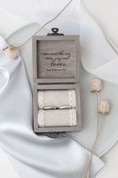 an open box with two wedding rings in it and some flowers on the table next to it