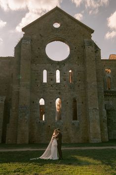 the bride and groom are standing in front of an old stone building with arched windows