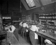 an old black and white photo of some women working in a kitchen with lots of bottles on the counter