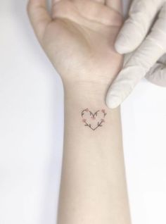 a small tattoo on the wrist of a person's hand, with two hearts in the middle