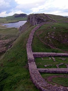 an old stone wall on the side of a hill next to a body of water