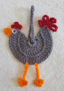 a crocheted chicken is sitting on a white surface with red and orange feathers